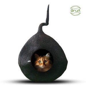 Może przedstawiać: Czarne filcowe legowisko dla kota w kształcie łzy z długim ogonem. Ruda kotka z zielonymi oczami zagląda przez otw&oacute;r.