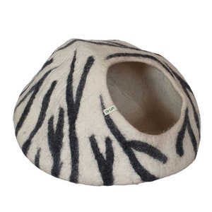 Może przedstawiać: Kojec dla kota z filcu w kolorze białym i czarnym z okrągłym otworem. Kojec ma zieloną etykietę z napisem "aruit".