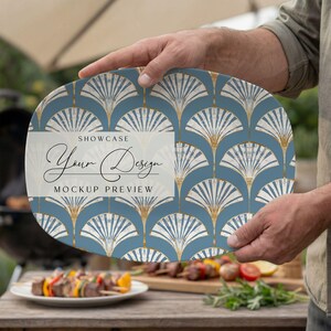 May include: An oval serving platter with a blue and gold art deco fan pattern. The platter has the text "SHOWCASE Your Design MOCKUP PREVIEW" in a white rectangle. The platter is being held outdoors near a grill.