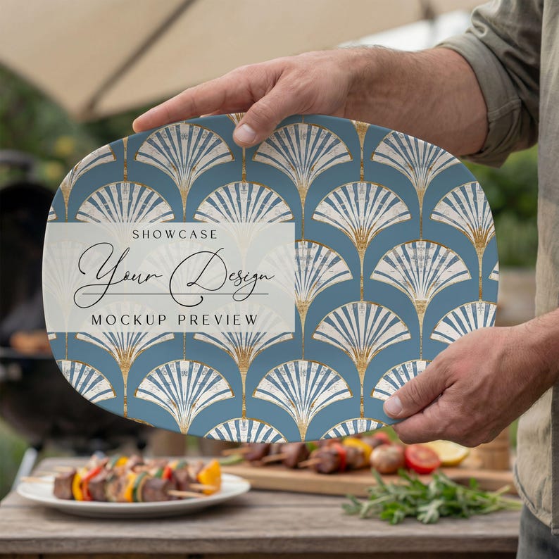 May include: An oval serving platter with a blue and gold art deco fan pattern. The platter has the text "SHOWCASE Your Design MOCKUP PREVIEW" in a white rectangle. The platter is being held outdoors near a grill.