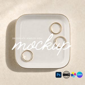 May include: A square white jewelry dish with a thin gold rim, featuring three gold rings placed on its surface. The text DECOPLATE JEWELRY DISH mockup is overlaid in white script across the center of the dish, with small software icons below.
