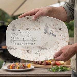 May include: An oval serving platter with a floral and bird design, held by a person. The platter features a cream background with illustrations of cranes and flowers. Text on the platter reads "Showcase Your Design Mockup Preview."