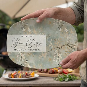 May include: An oval-shaped serving platter with a floral and bird design, held by a person. The platter has a light blue and beige background with white flowers and small birds. The text "SHOWCASE Your Design MOCKUP PREVIEW" is displayed on the platter.