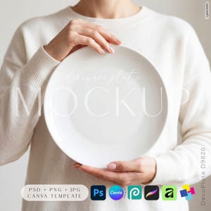 May include: A plain white ceramic plate held in front of a cream-colored sweater. The plate features a smooth, circular surface with a wide rim. Text overlay on the plate reads "decorware plate MOCKUP" in a light, elegant script and sans-serif font.