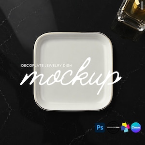 May include: A square white jewelry dish with a thin gold-colored rim. The text DECORATE JEWELRY DISH mockup is printed in white across the center of the dish. The dish has rounded corners and a smooth, glossy finish, presented from a top-down view.