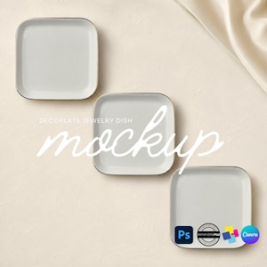 May include: Three square white jewelry dishes with rounded corners and thin metallic rims arranged in a diagonal pattern. The text DECOPLATE JEWELRY DISH mockup is overlaid in white script, with small software and brand logos in the bottom corner.
