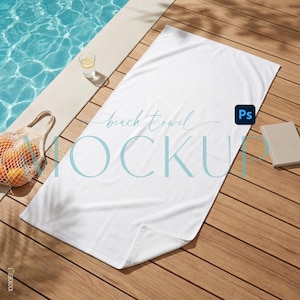 May include: A white beach towel mockup with the text "beach towel MOCKUP" in light blue. The towel is on a wooden deck next to a pool. A glass of water and a bag of oranges are also visible.