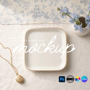 May include: A square white ceramic jewelry dish with a thin gold rim. The dish features the text DECORATE JEWELRY DISH mockup in white script. A gold locket necklace lies to the left of the dish on a white fabric surface with a blue floral pattern.