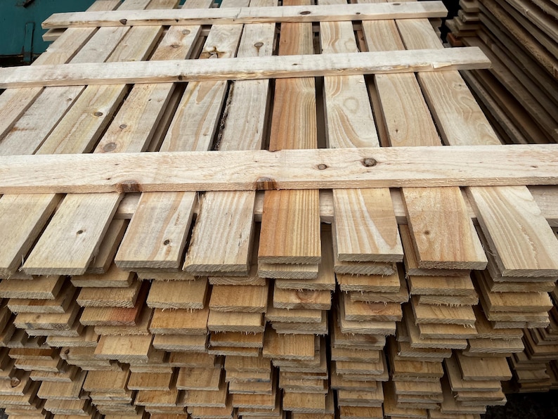 May include: A stack of unfinished wooden pallets. The pallets are made of light-colored wood with visible grain and knots. The boards are arranged in a grid pattern, with horizontal and vertical planks.