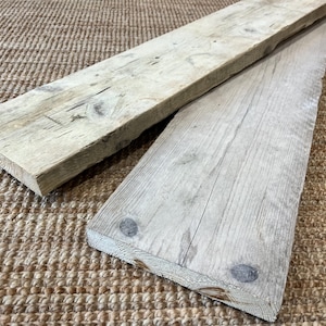 May include: Two rectangular wooden boards with a weathered, light gray finish. The boards feature visible wood grain, natural knots, and rough, textured surfaces. The wood displays signs of age with subtle cracks and variations in color tone.