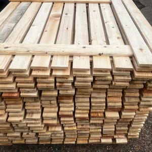 May include: A stack of unfinished wooden planks, varying in shades of light brown and tan. The planks are arranged in a neat, organized pile, with some planks forming a top layer. The wood appears to be new and ready for use in a construction or craft project.