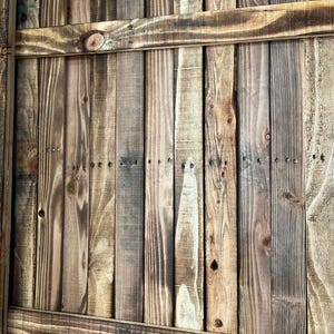 May include: A close-up of a wooden fence made of horizontal planks. The wood is a mix of brown and light brown, with some darker areas. The planks are nailed together with small nails.