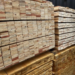 May include: Stacks of freshly cut lumber, showcasing the natural grain and color variations of the wood. The lumber is neatly arranged in layers, ready for construction or woodworking projects. The wood appears to be pine or a similar softwood.