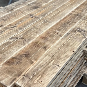 May include: Stack of reclaimed wood planks, showing the natural grain and knots. The wood has a rustic, weathered look with a light brown colour.