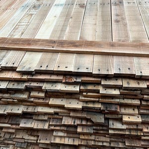 May include: A stack of reclaimed wood planks, some of which are nailed together to form a larger panel. The wood is a mix of light and dark brown tones, with a weathered and rustic appearance.