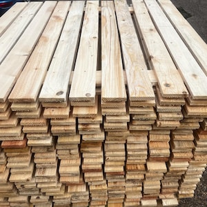 May include: A stack of unfinished wooden planks, showing the natural grain and color variations of the wood. The planks are arranged in layers, creating a textured surface. The wood appears to be new and ready for use in a variety of projects.