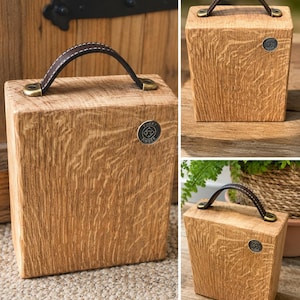 Puede incluir: Un tope de puerta rectangular de madera de roble claro con un asa de cuero marr&oacute;n oscuro sujeta con herrajes de lat&oacute;n antiguo. Una peque&ntilde;a insignia met&aacute;lica circular con el texto Funky Timber est&aacute; incrustada en la cara frontal del bloque.
