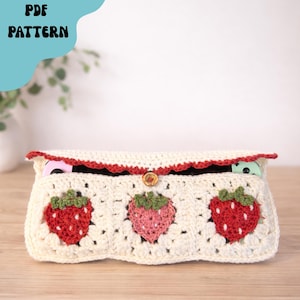 Puede incluir: Bolso de mano de ganchillo color crema con tres aplicaciones de fresas. Las fresas son rojas y rosas con hojas verdes. El bolso tiene un ribete festoneado rojo y un cierre de botón. El texto "PDF PATTERN" está en la esquina superior izquierda.