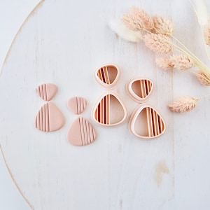 Op de afbeelding: Een set van vier roze polymer clay oorbellen met een geometrisch ontwerp. De oorbellen hebben de vorm van een traan met een gestreept patroon. De oorbellen worden gepresenteerd op een wit houten oppervlak.