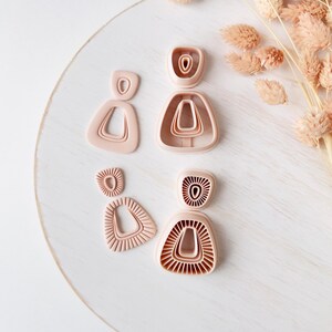 Peut inclure: Un ensemble de quatre emporte-pièces en plastique rose clair pour argile aux formes géométriques. Deux emporte-pièces présentent des contours lisses, triangulaires et ovales, tandis que les deux autres ont des motifs striés.