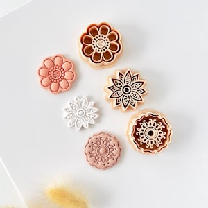 Könnte beinhalten: Eine Sammlung von Ausstechern in Blumenform in verschiedenen Farben, darunter Pfirsich, Weiß und Braun. Die Ausstecher weisen detaillierte Blumendesigns auf, ideal zum Backen und Basteln. Auf weißem Hintergrund angeordnet.