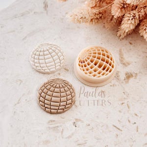 Könnte beinhalten: Drei beige Globus-Ausstecher. Einer ist ein kompletter Globus, ein anderer ein globusförmiger Ausstecher und der dritte ein globusförmiger Abdruck. Der Text "Paulas Cutters" ist im Bild sichtbar.
