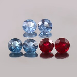Könnte beinhalten: Fünf facettierte Edelsteine, zwei blaue und drei rote, in einer Reihe auf einer reflektierenden Oberfläche angeordnet.