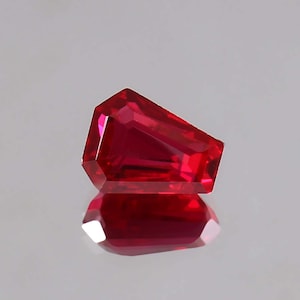 Könnte beinhalten: Ein tief roter Edelstein mit einer facettierten, achteckigen Form. Der Edelstein ist in einem einzigartigen, asymmetrischen Stil geschliffen.
