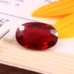 Könnte beinhalten: Ein ovaler Edelstein in tiefroter Farbe mit einem facettierten Schliff.