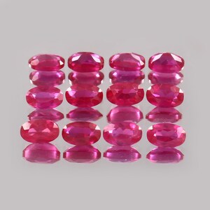 Könnte beinhalten: Eine Ansammlung von sechzehn oval geschliffenen Rubinen, angeordnet in vier Spalten zu je vier. Die Edelsteine haben eine lebendige, tiefrote Farbe mit einer polierten, reflektierenden Oberfläche. Jeder Rubin ist in etwa gleich groß und geformt.