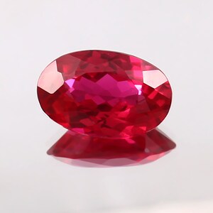 Könnte beinhalten: Ein leuchtend roter ovaler Edelstein mit facettiertem Schliff. Der Edelstein reflektiert das Licht und zeigt seine Brillanz.