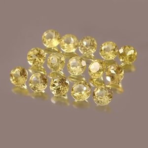 May include: A group of 15 yellow gemstones, likely citrine, arranged in a loose cluster on a gray background.