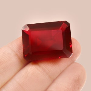 Könnte beinhalten: Ein tief roter Edelstein mit einem rechteckigen Smaragdschliff. Der Edelstein wird in einer Hand gehalten.