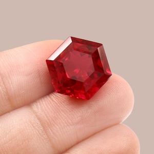 Könnte beinhalten: Ein tief roter Edelstein mit sechseckigem Schliff, in einer Hand gehalten.