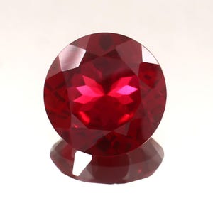 Op de afbeelding: Een dieprode edelsteen met een ronde vorm en vele facetten. De edelsteen reflecteert licht en heeft een glanzende afwerking.