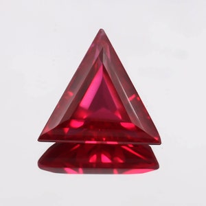 Könnte beinhalten: Ein dreieckiger Rubin-Edelstein in tiefroter Farbe. Der Edelstein ist facettiert und hochglanzpoliert.