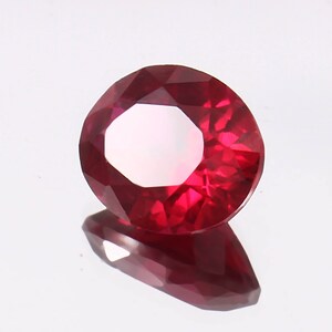 May include: A deep red gemstone with a faceted cut. The gemstone is round and has a high polish.