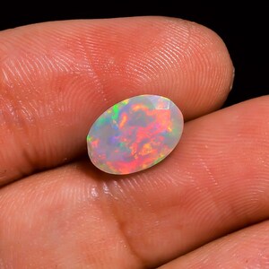 Könnte beinhalten: Ovaler Opal-Edelstein mit weißer Basis und schillernden Farbschichten in Rosa, Orange und Grün.