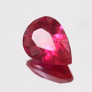 Könnte beinhalten: Ein birnenförmiger Rubin-Edelstein mit einer tief roten Farbe. Der Edelstein ist facettiert und hat einen hohen Grad an Brillanz.