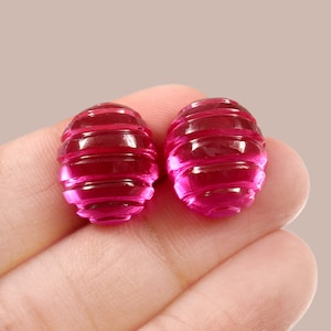 Könnte beinhalten: Zwei ovale, rosafarbene, facettierte Edelsteine mit einem gerippten Design.