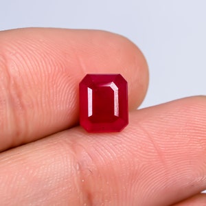 Könnte beinhalten: Ein tiefroter Smaragdschliff-Edelstein, der in einer Hand gehalten wird.