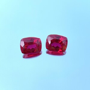 Könnte beinhalten: Zwei rote Kissen-Schliff-Edelsteine auf blauem Hintergrund.