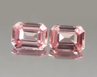 May include: Two pink emerald cut gemstones, each with a rectangular shape and a smooth, polished surface.