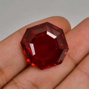 Könnte beinhalten: Ein tief roter, achteckiger Edelstein mit facettiertem Schliff.