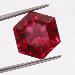 May include: A deep red gemstone with a hexagonal cut and a star-shaped pattern in the center.