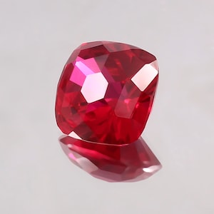 Könnte beinhalten: Ein tiefroter Edelstein mit einem Kissen-Schliff. Der Edelstein ist facettiert und hat einen hohen Glanz.