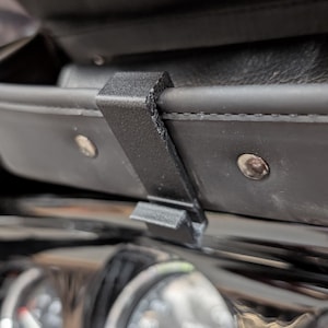 May include: A black plastic clip designed to hold a phone or other device in a motorcycle's storage compartment.