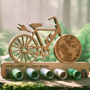 Puede incluir: Soporte de dinero de madera con forma de bicicleta con un globo en la rueda trasera y un diseño de enchufe en la delantera. La base tiene el texto "HERZLICHEN GLÜCKWUNSCH" y contiene billetes enrollados. Fondo verde borroso.