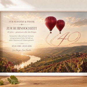 Op de afbeelding: Een ingelijste print met een landschap van een rivier die door wijngaarden slingert bij zonsondergang. Twee rode heteluchtballonnen zweven in de lucht, met rooksporen die het getal 40 vormen. De tekst luidt: FÜR SUSANNE & FRANK ZUR RUBINHOCHZEIT 40 Jahre.