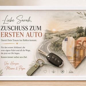 Può includere: Una cornice bianca con un'illustrazione paesaggistica di una strada, una chiave dell'auto con un portachiavi verde salvia e una banconota da 50 euro piegata a forma di cuore. Il testo recita: Liebe Sarah, ZUSCHUSS ZUM ERSTEN AUTO, Damit Dein Traum ins Rollen kommt.